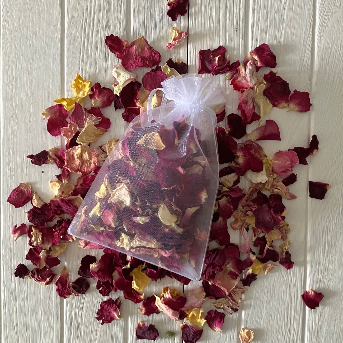 Bag of dried rose petals on a white wooden surface